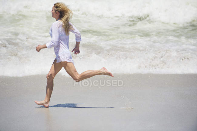 Блондинка в рубашке бегает по пляжу — стоковое фото