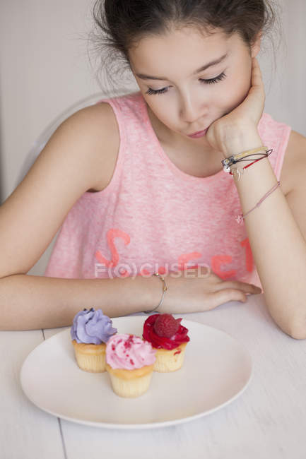 Chica pensativa mirando cupcakes en la mesa - foto de stock
