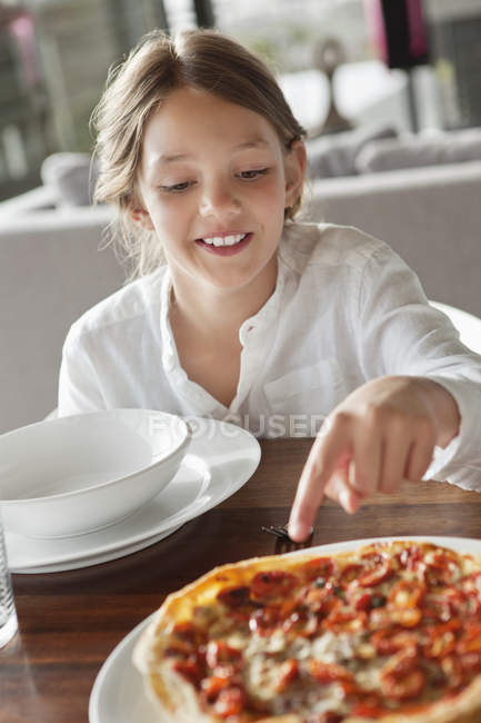 Усміхнена дівчинка сидить за дерев'яним столом з їжею і вказує на їжу — стокове фото