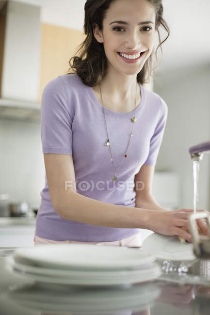 Femme laver la vaisselle dans la cuisine et regarder la caméra — Photo de stock