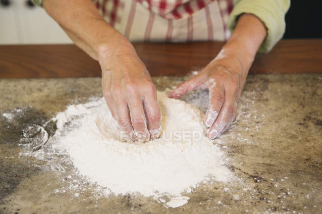 Gros plan des mains féminines mélangeant la farine sur le comptoir de la cuisine — Photo de stock