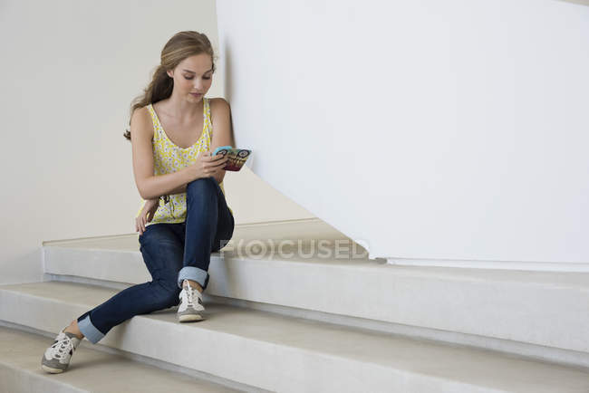 Chica adolescente sentada en los escalones y usando un teléfono inteligente - foto de stock
