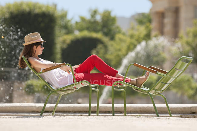 Жінка в солом'яному капелюсі відпочиває в кріслі біля ставка — стокове фото