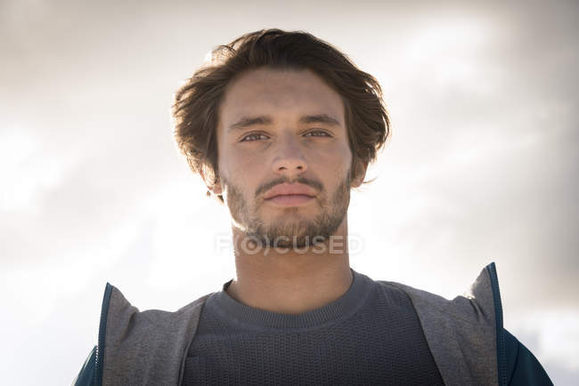 Retrato del joven mirando a la cámara contra el cielo nublado - foto de stock
