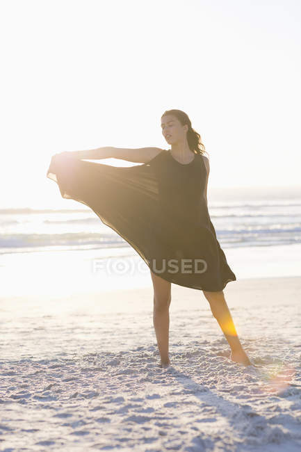 Молода жінка в чорній сукні позує на пляжі — стокове фото