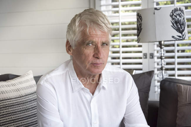 Portrait of senior man in white shirt sitting at home — Stock Photo