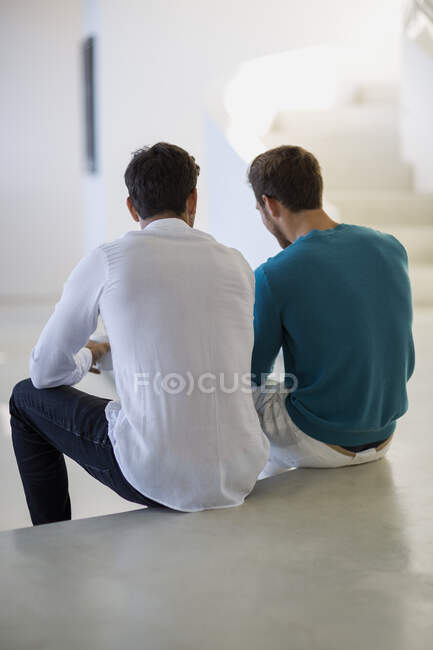 Vista trasera de dos amigos varones sentados en el suelo - foto de stock