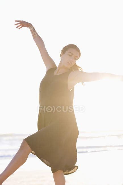 Mujer joven en vestido negro posando en la playa con las manos levantadas - foto de stock