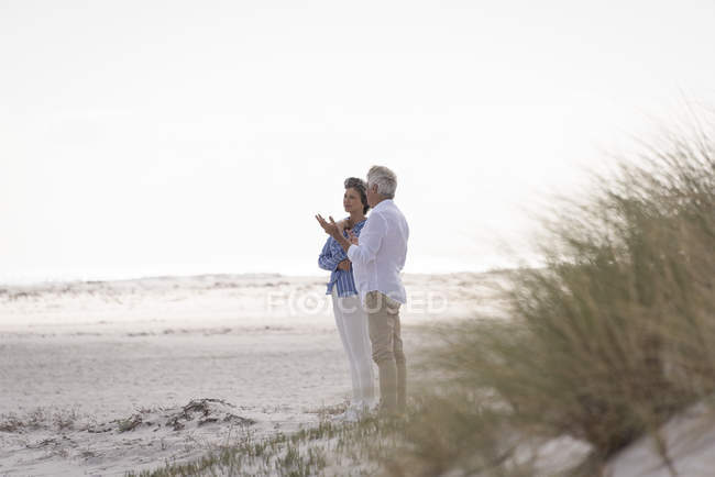 Счастливая старшая пара разговаривает на песчаном пляже — стоковое фото