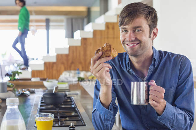 Hombre desayunando en el mostrador de la cocina y mirando a la cámara - foto de stock
