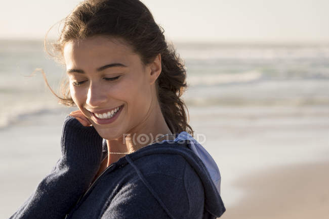 Lächelnde junge Frau im Kapuzenpulli blickt auf den Strand — Stockfoto