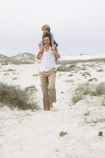Homme portant son fils sur ses épaules sur la plage — Photo de stock