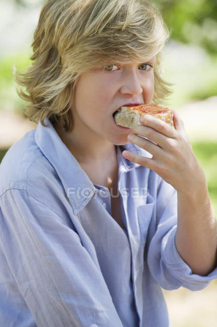Хлопчик з білявим волоссям їсть бутерброд на відкритому повітрі — стокове фото