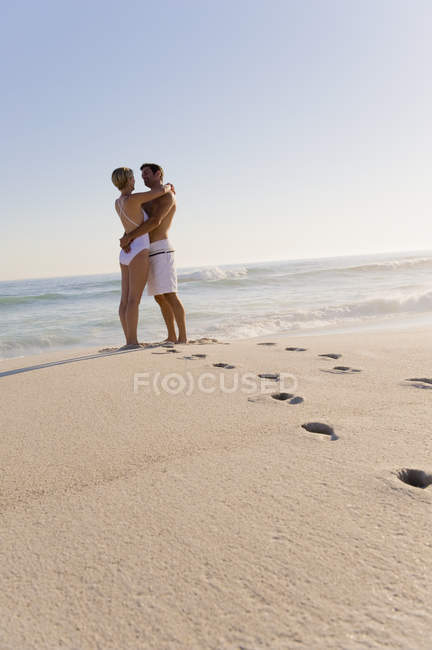 Footprints on sandy beach with couple standing on background and looking at each other — Stock Photo