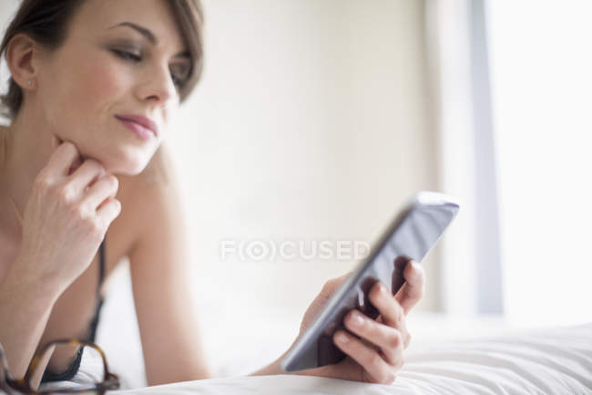Mujer sonriente acostada en la cama y usando el teléfono móvil - foto de stock