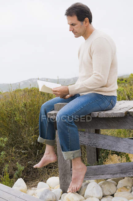 Man sitting on boardwalk in nature and reading a book — Stock Photo