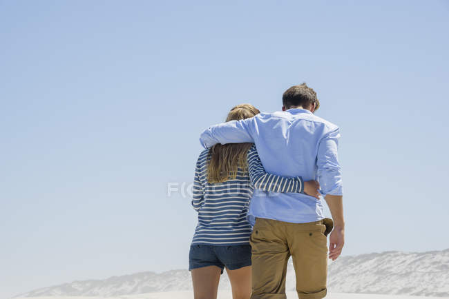 Вид сзади на романтическую пару, гуляющую по пляжу под голубым небом — стоковое фото