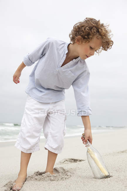 Menino chegando para mensagem em uma garrafa na praia de areia — Fotografia de Stock