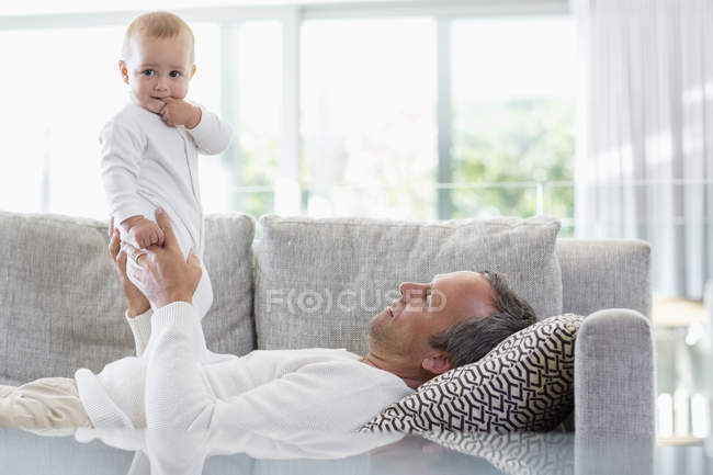 Buon padre sdraiato sul divano e giocare con la figlia bambino carino a casa — Foto stock