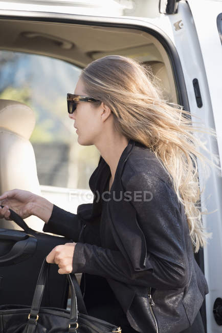 Elegante mujer de negocios en gafas de sol poniendo equipaje en el coche - foto de stock