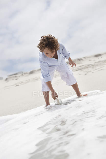 Boy putting bottle with message in water on beach — Stock Photo