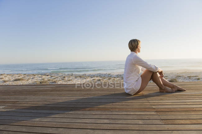 Entspannte Frau sitzt auf der Strandpromenade am Meer und blickt auf die Aussicht — Stockfoto