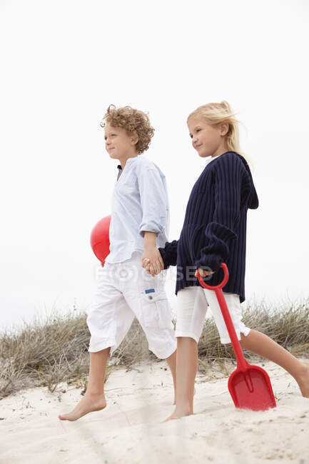 Брат и его сестра ходят по песку, держась за руки — стоковое фото