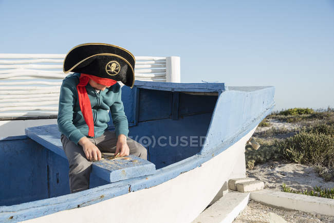 Pirate little boy counting coins on wooden boat outdoors — Stock Photo