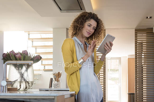 Mujer reflexiva utilizando tableta digital en la cocina - foto de stock