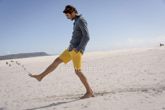 Joyeux jeune homme donnant des coups de pied de sable sur la plage — Photo de stock