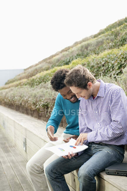 Amigos discutiendo documentos en un paseo marítimo - foto de stock