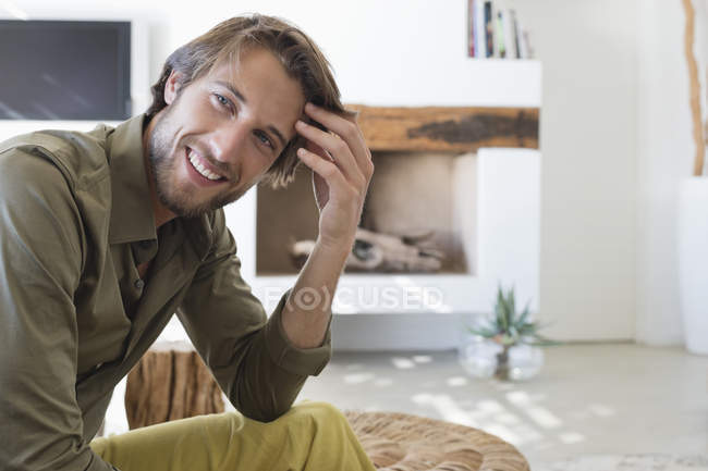 Porträt eines hübschen Mannes, der im Wohnzimmer sitzt und lächelt — Stockfoto
