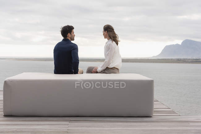 Vista posteriore della coppia seduta sul pouf al lago e guardando la vista — Foto stock