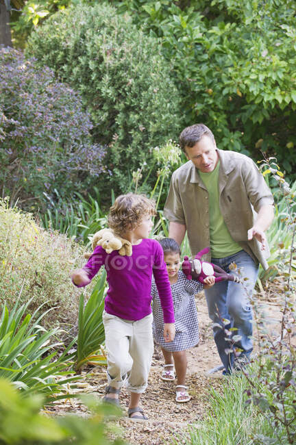 Отец с двумя детьми, гуляющими в саду — стоковое фото