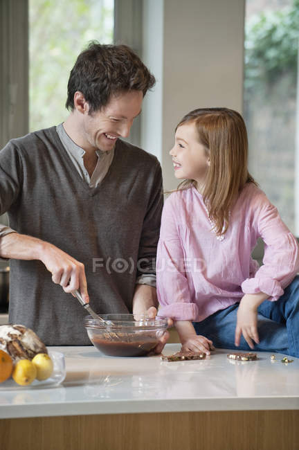 Uomo mescolando miscela in ciotola con figlia in cucina — Foto stock