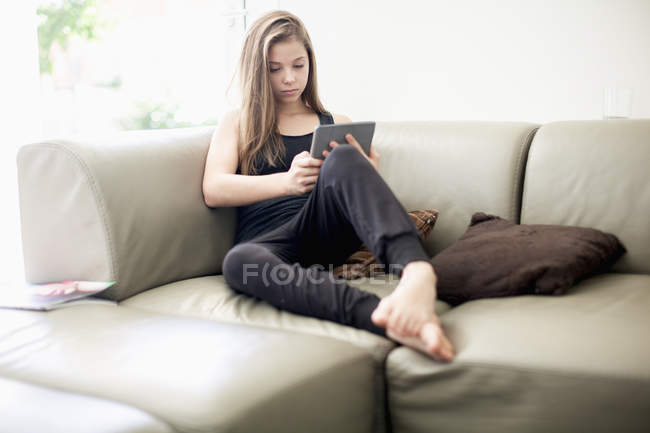 Девочка-подросток с помощью цифрового планшета на диване дома — стоковое фото