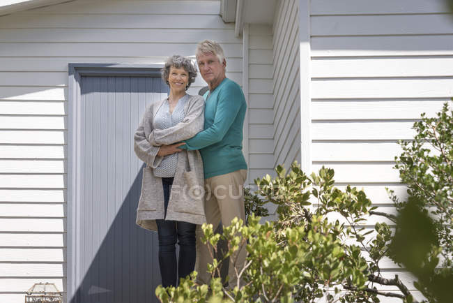 Portrait of happy senior couple embracing outside of house — Stock Photo