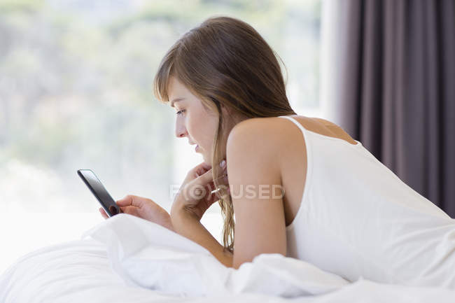 Молода жінка обміну повідомленнями з мобільним телефоном в ліжку — стокове фото