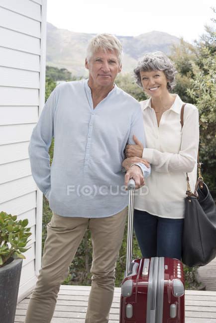 Щаслива пара старший стоячи з чемодан поза домом і дивлячись на камеру — стокове фото