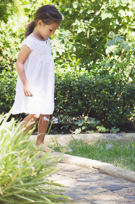 Menina no vestido de verão branco andando no jardim ensolarado — Fotografia de Stock