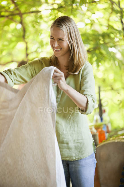Sorrindo mulher segurando toalha de mesa no jardim — Fotografia de Stock