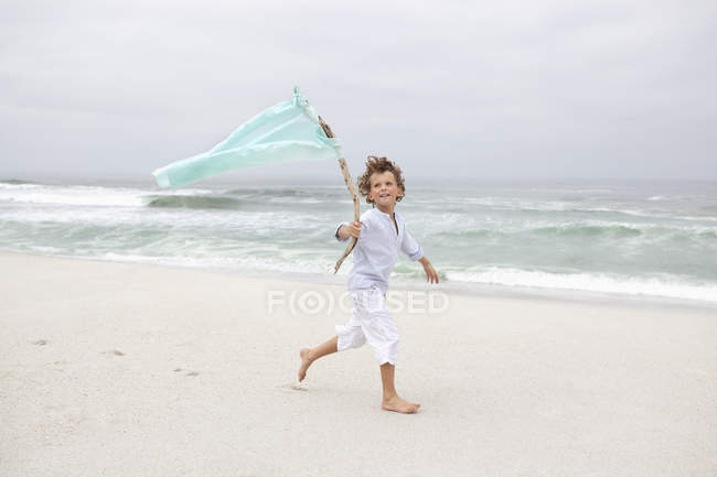 Boy running while holding flag on sandy beach — Stock Photo
