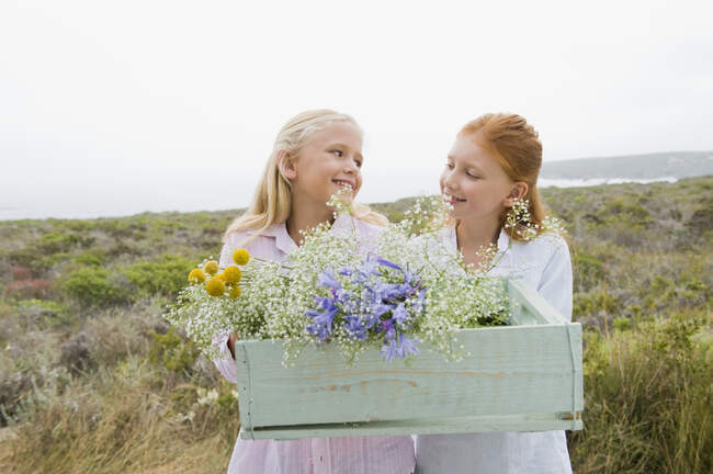 Dos chicas llevando una caja de flores y sonriendo - foto de stock