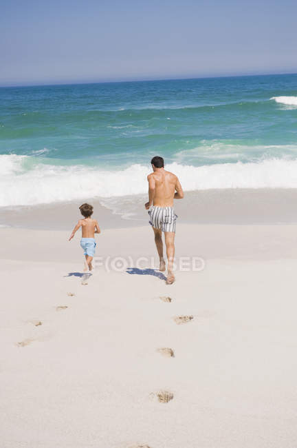 Чоловік біжить з сином на піщаному пляжі — стокове фото