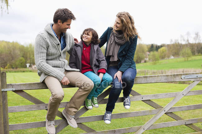 Хлопчик сидить з батьками на дерев'яному паркані в сільській місцевості — стокове фото