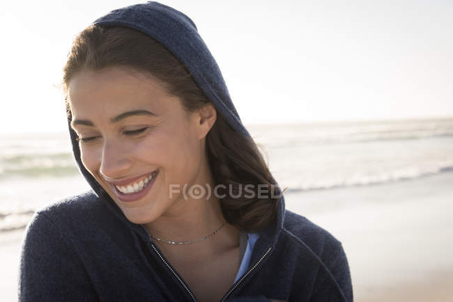 Primer plano de la joven sonriente en chaqueta con capucha en la playa - foto de stock
