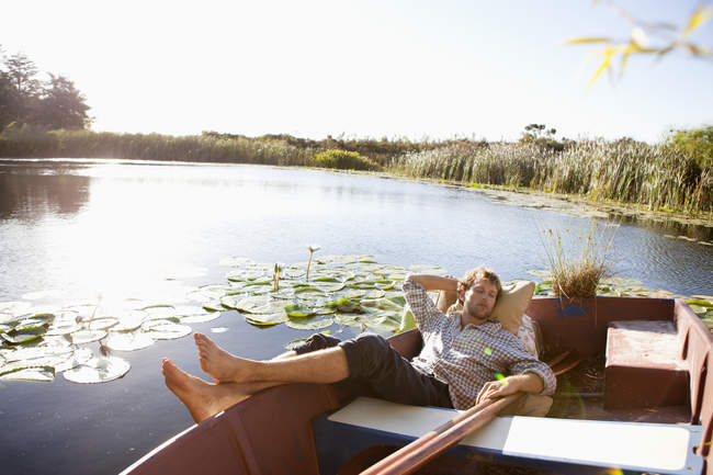 Relaxado jovem dormindo em barco no lago no campo — Fotografia de Stock