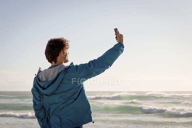 Happy young man taking selfie with camera phone on beach — Stock Photo