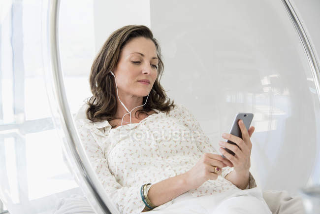 Mature woman listening to music with smartphone in chair — Stock Photo