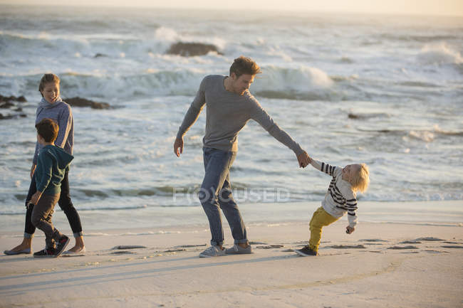 Familia divirtiéndose en la playa de arena al atardecer - foto de stock